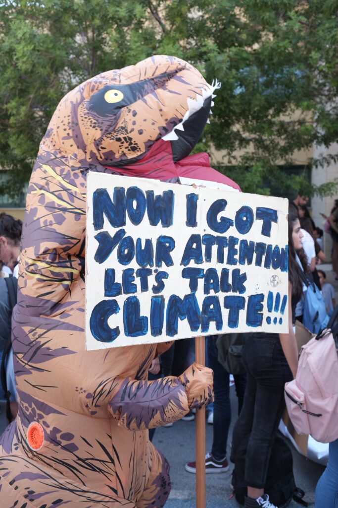 Dino holds sign "Let's Talk Climate"
